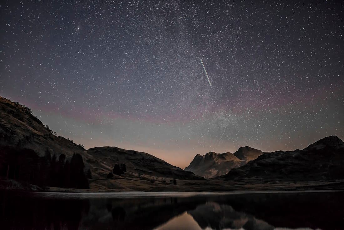 A meteor streaking across a star-filled night sky above dark, silent mountains.